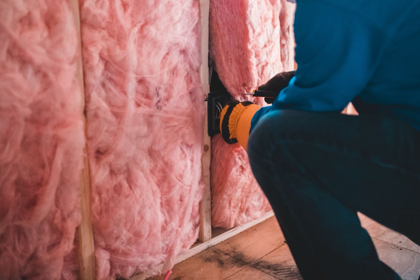 Installer fitting pink fiberglass insulation batts between studs